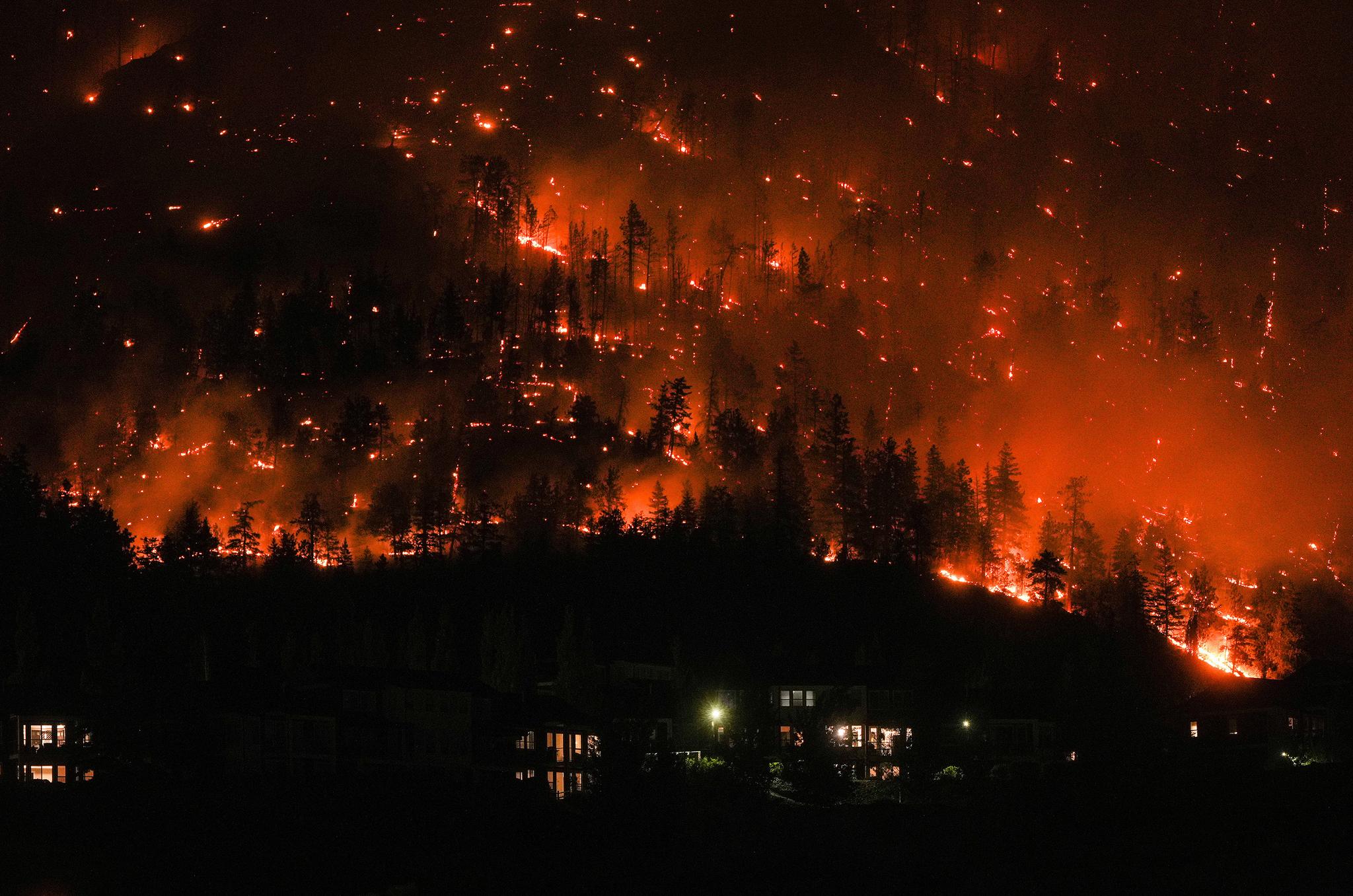 A mountain town with the forest behind it on fire.