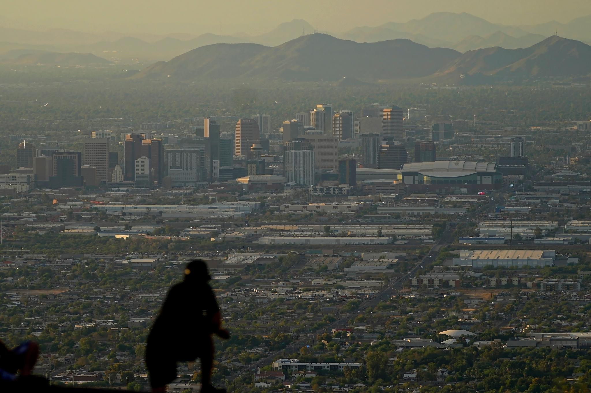 A man overlooks downtown Phoenix at sunset atop South Mountain, Sunday, July 30, 2023