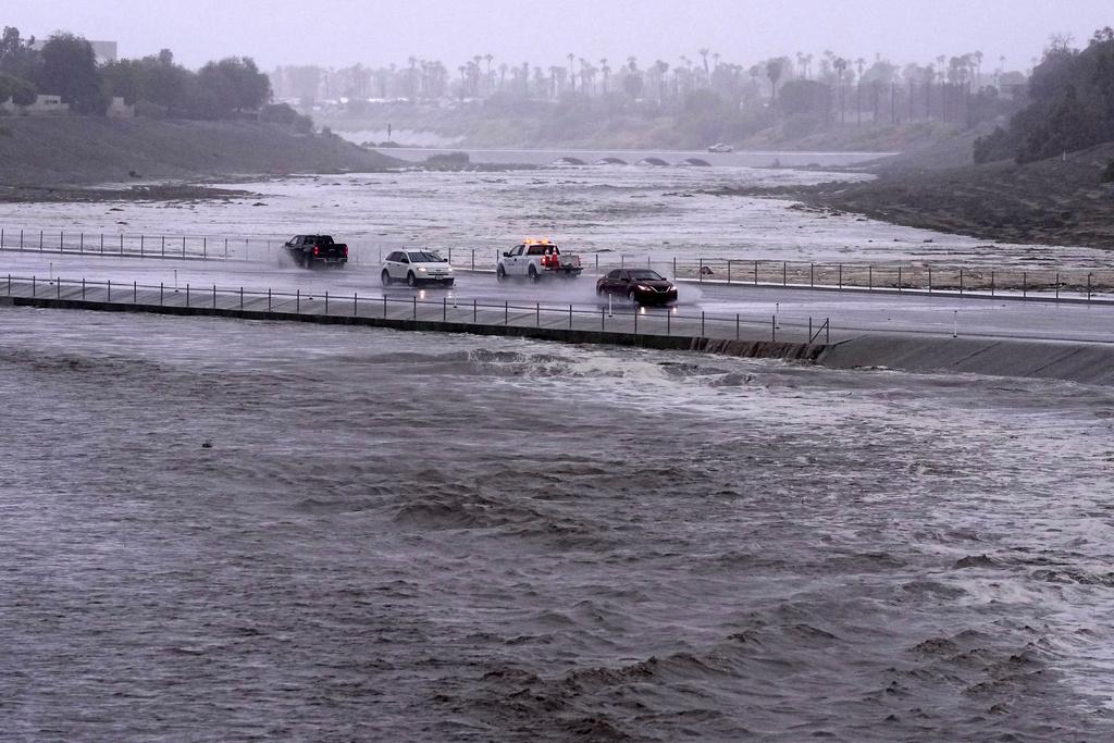 Vehicles cross over a flood control basin that has almost reached the street