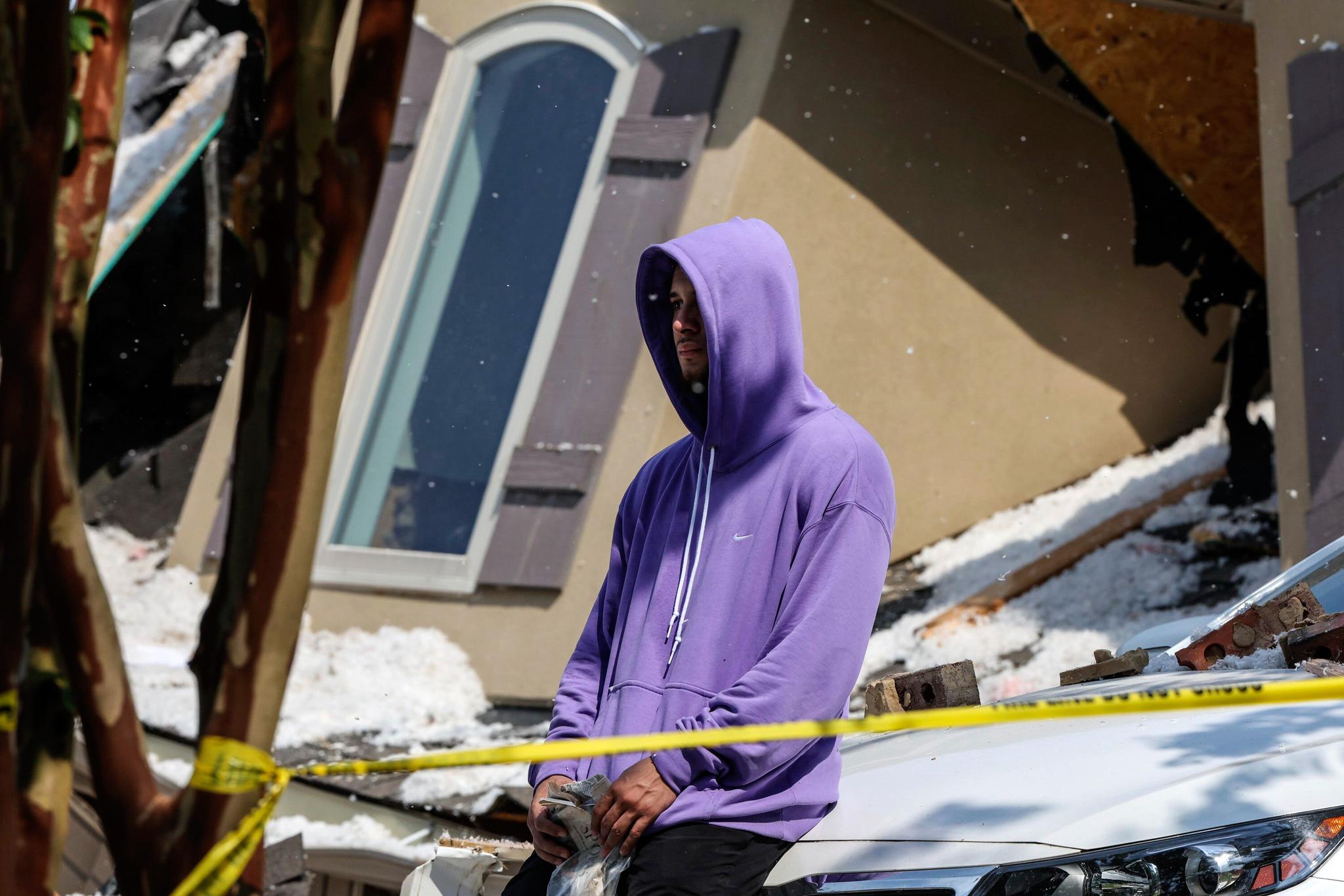 Man in purple hoodie with hood up in front of exploded house
