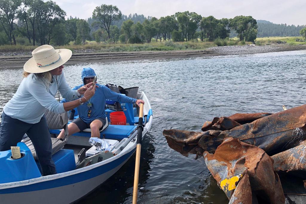 Wendy Weaver with Montana Freshwater Partners, left, photographs a piece of a railroad tank car in the Yellowstone River, Monday, Aug. 21, 2023
