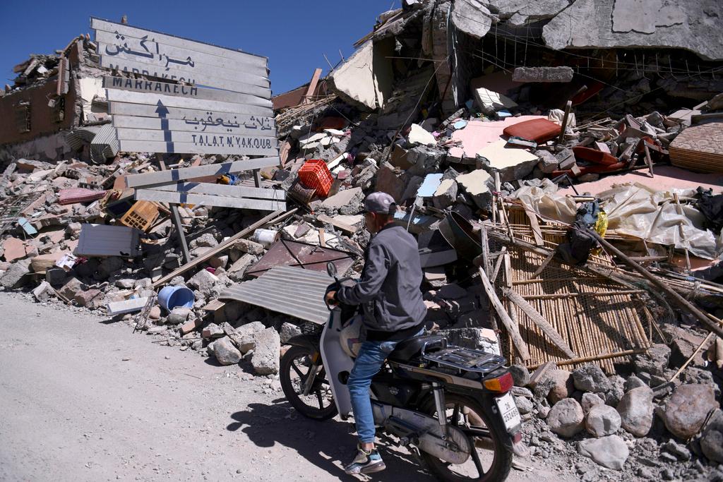 A man on a scooter drives past rubble and a damaged road sign pointing to Marrakech in Talat N'yakoub, Morocco, Monday Sept. 11, 2023.