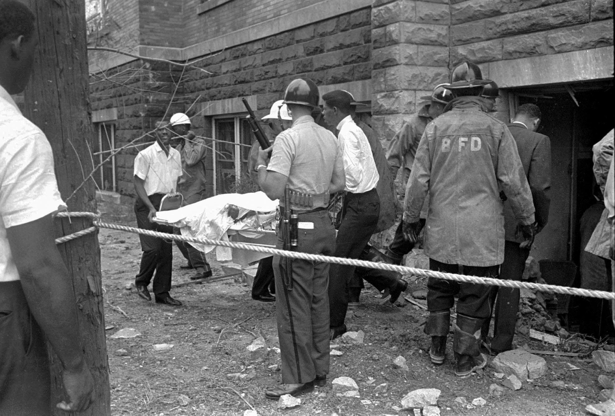 Church members carrying out a body on a stretcher with firefighters surrounding the bombed areas.