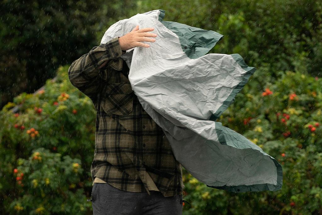 Man struggles with his rain poncho in strong wind as weather associated with Storm Lee in Maine