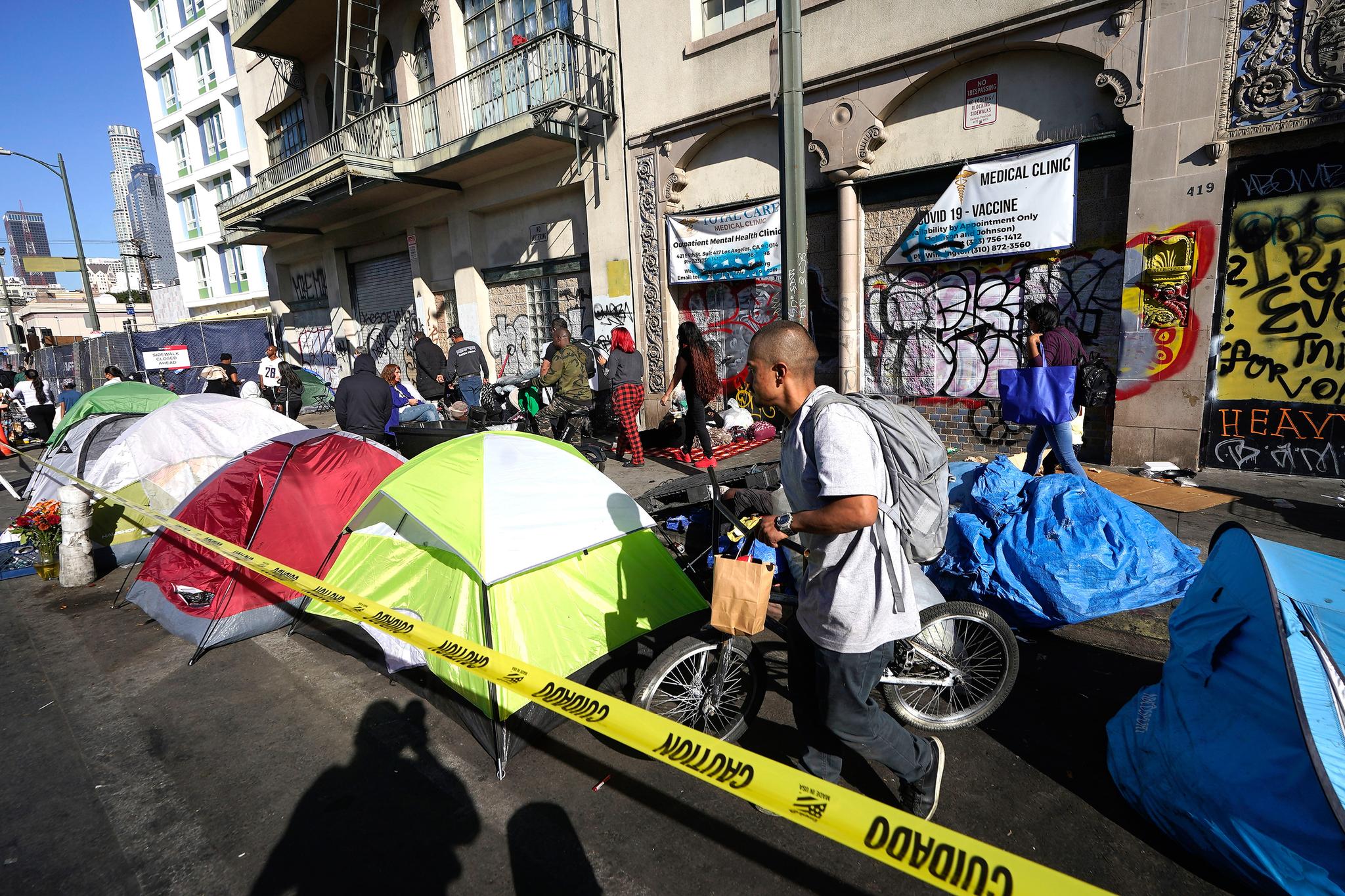Man steers his bicycle past a bunch of tents on skid row.