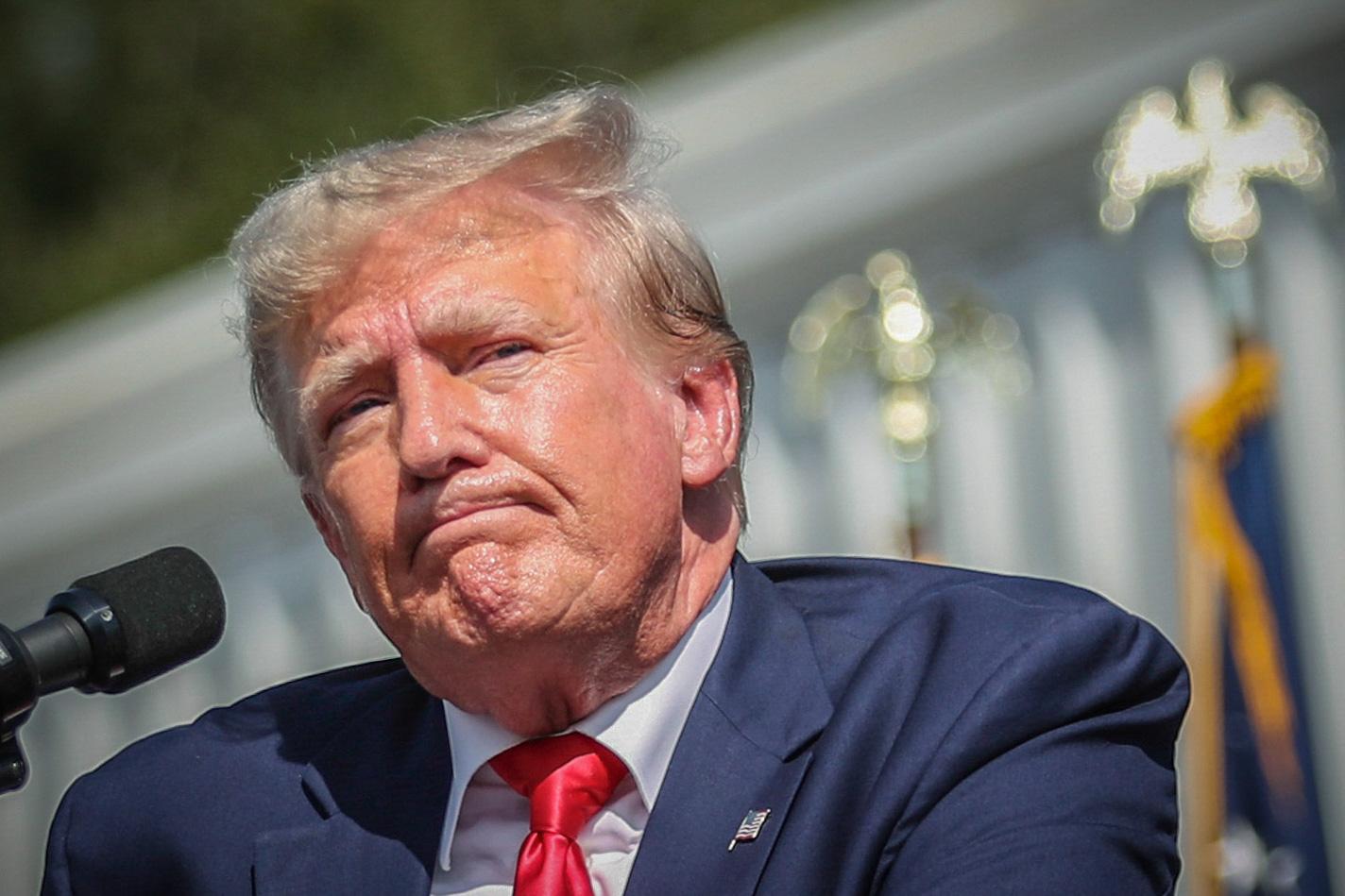 Former Pres.  Trump at a microphone, pressing his lips together