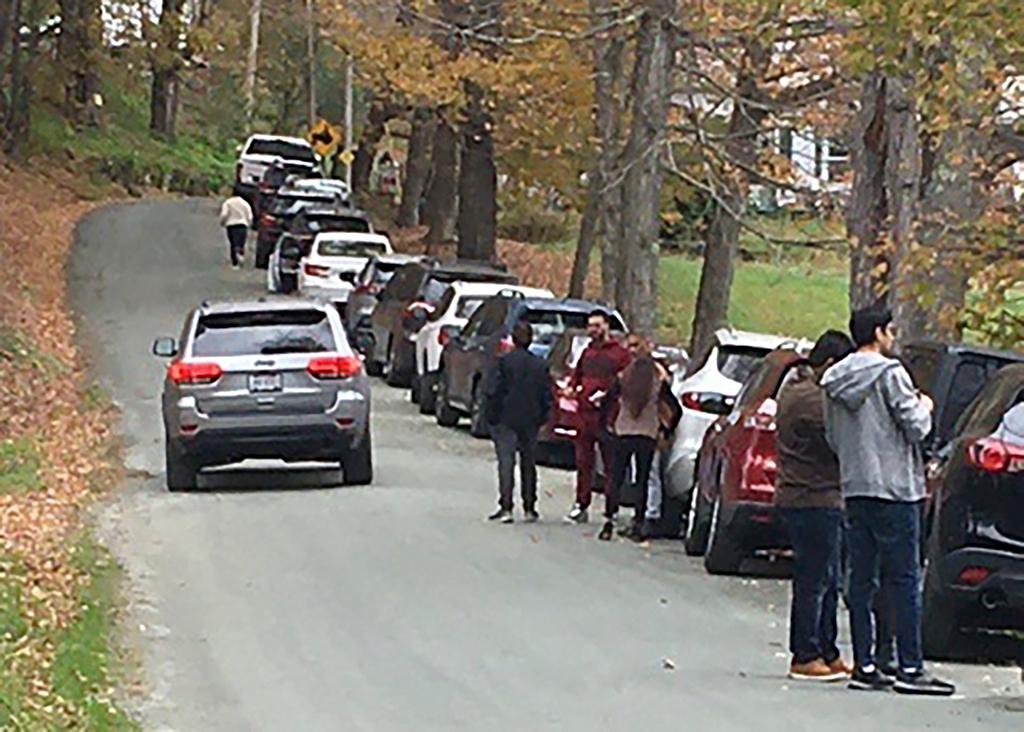 People and cars line a narrow road outside a private property in Pomfret, Vt., that has become a destination for fall foliage viewers, clogging the rural road. 