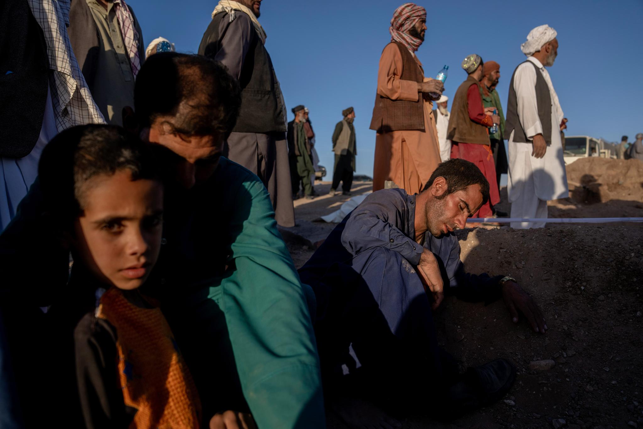 A child in the foreground as men are in the background near a grave.