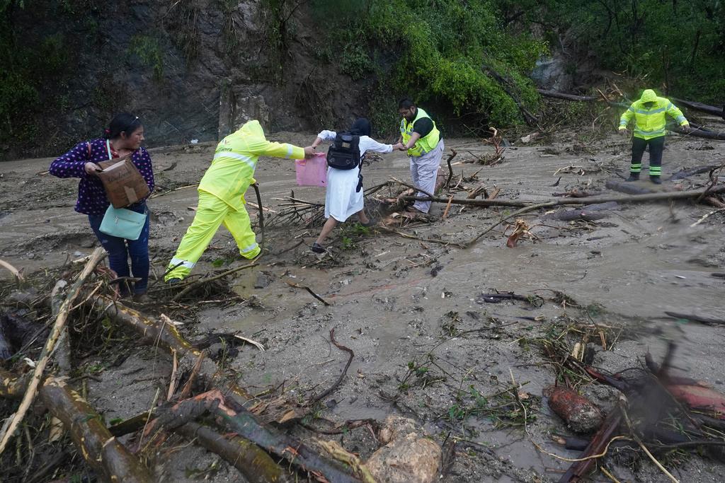People are helped as they cross a highway blocked by a landslide triggered by Hurricane Otis 