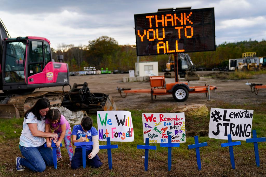 Bre Allard, accompanied by her children Lucy, 5, and Zeke, 8, plant crosses in honor of lives lost in Lewiston, Maine