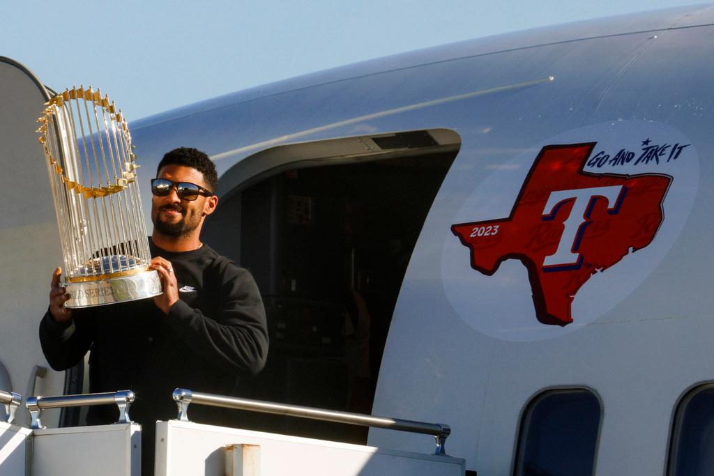 Texas Rangers' Marcus Semien hoists the Commissioner's Trophy next to pitcher José Leclerc upon the arrival of the baseball team at Dallas Love Field on Thursday, Nov. 2, 2023, in Dallas