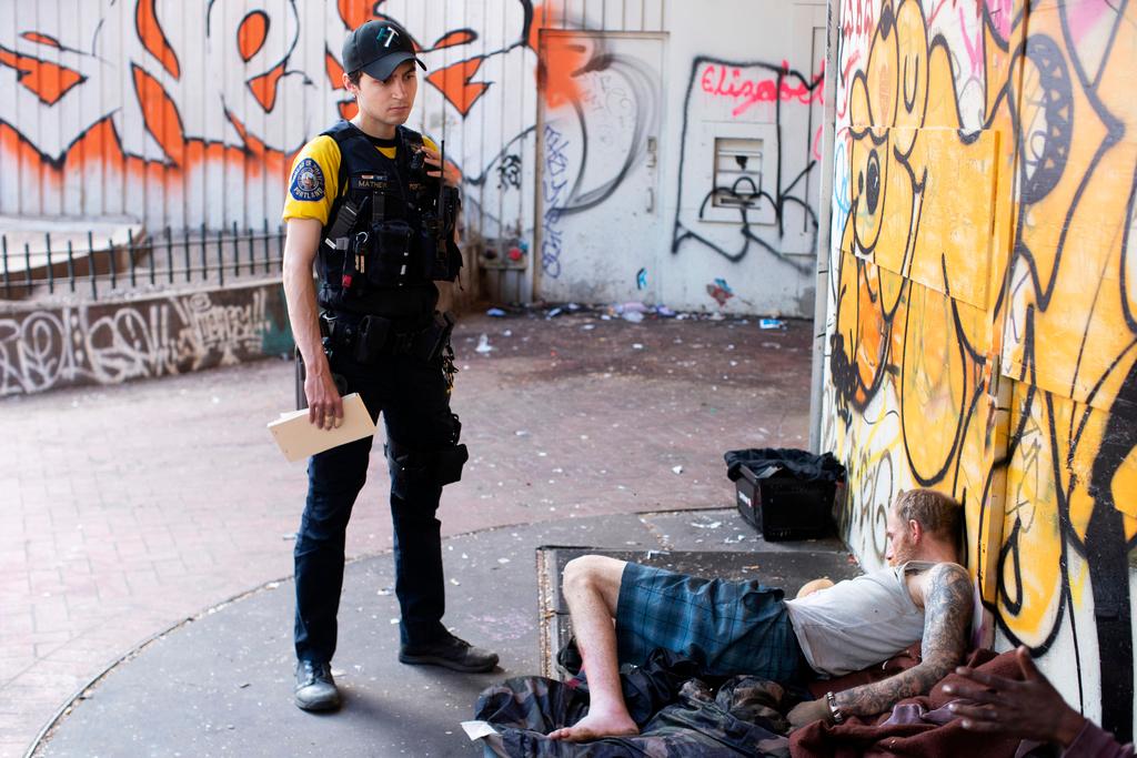 Officer Donny Mathew of the Portland Police Bureau's bike squad, stands next to a person who passed out in downtown Portland, Ore. 