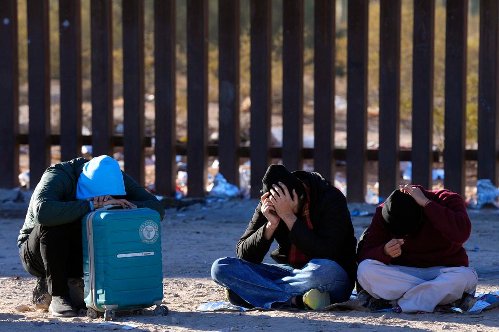 Undocumented migrants rest in the desert along the border wall 
