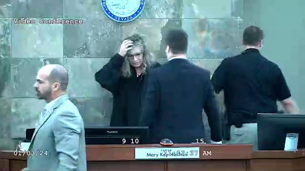 In this image from video provided by the Clark County District Court, Judge Mary Kay Holthus is seen cradling her head after a defendant launched over her desk during his sentencing in a felony battery case, Wednesday, Jan. 3, 2024 in Las Vegas.