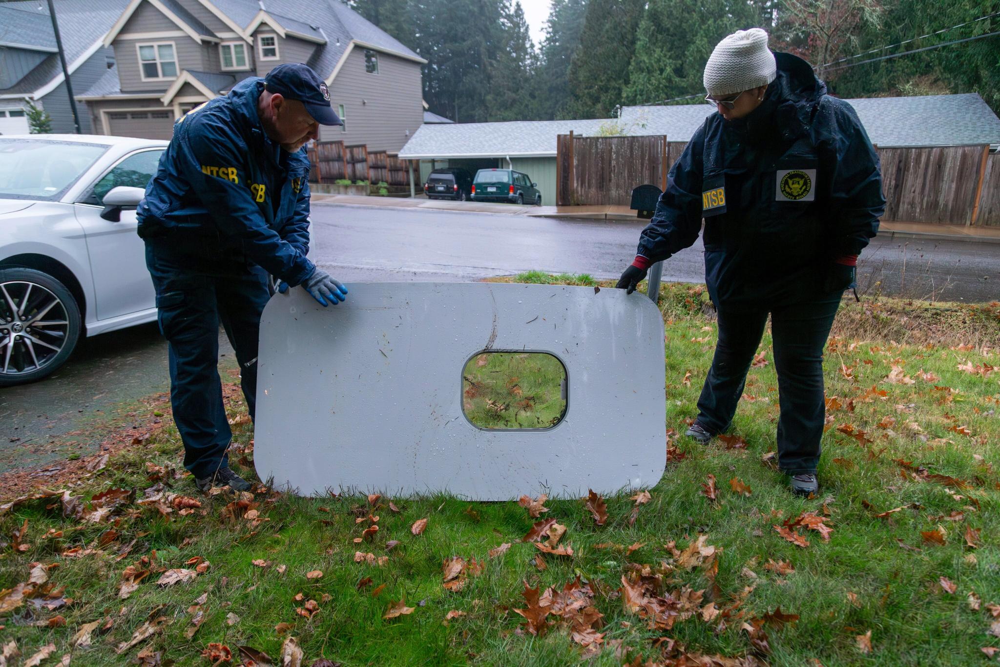 Two NTSB agents holding up an airline door that feel in someone's front yard