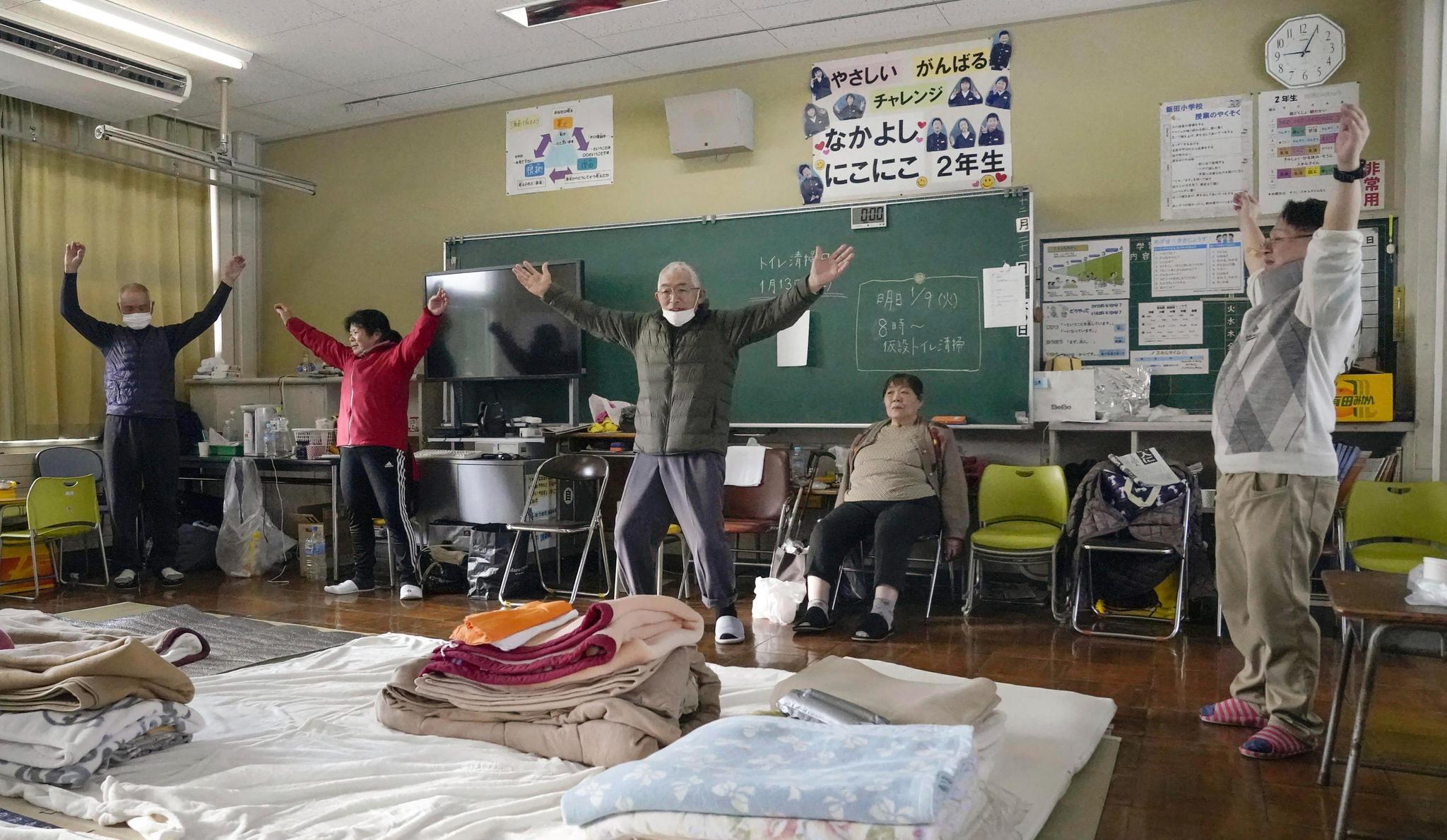 Men and women doing tai chi in a classroom with shelter bedding on the floor.