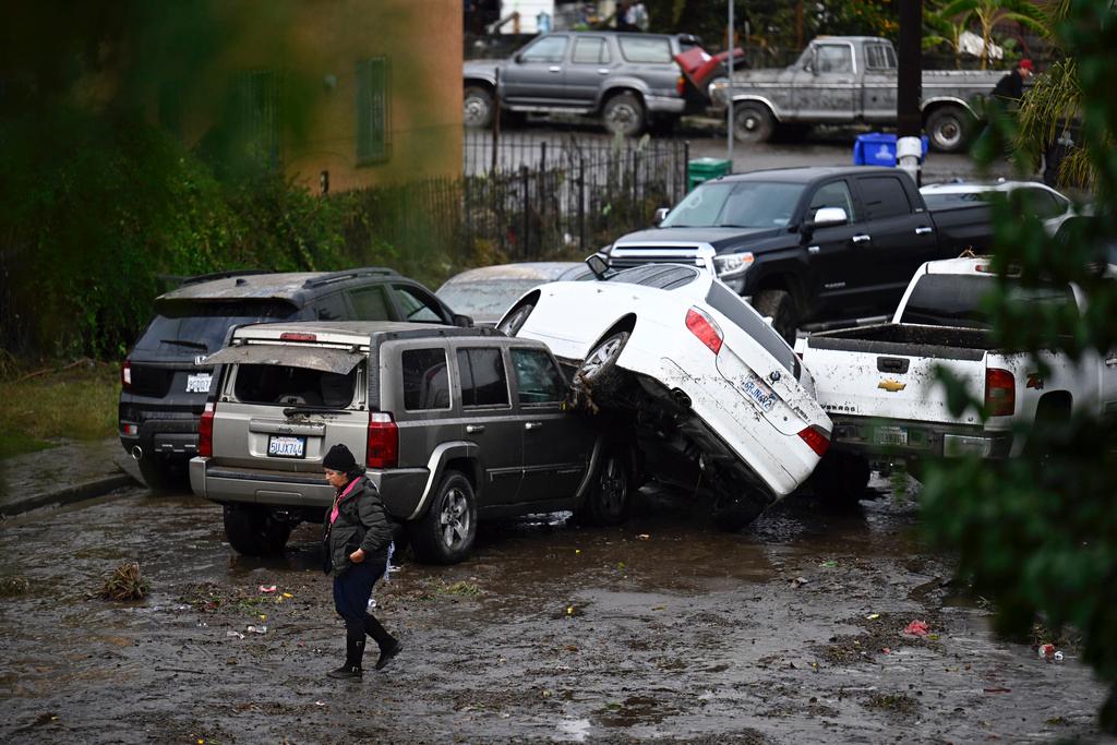 Woman walks by cars damaged from floods during a rain storm