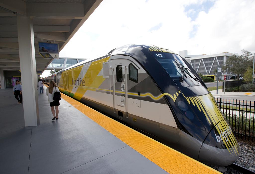 People walk near a Brightline train at a station
