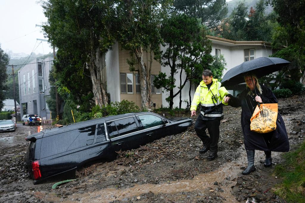 First responder helps a resident evacuate from a neighborhood after a mudslide in the Beverly Crest area of Los Angeles