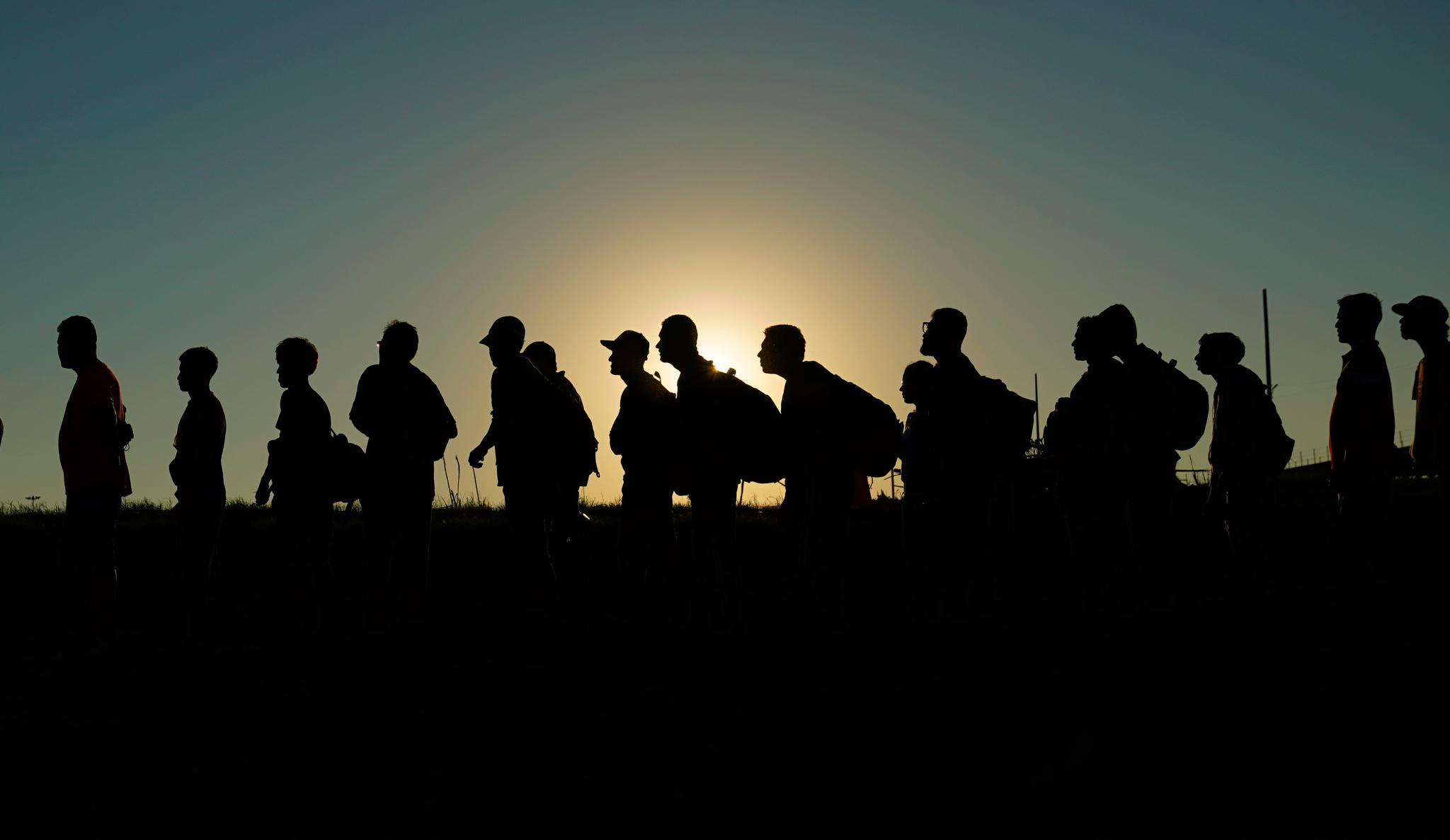 People walking in a line along a path with the late afternoon sun behind them.
