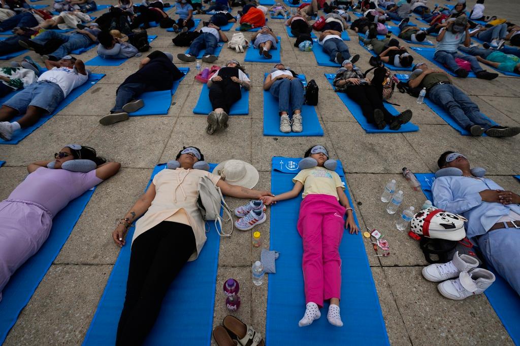 Lolling with bright blue mats, sleeping masks and travel pillows, people lie sprawled out 
