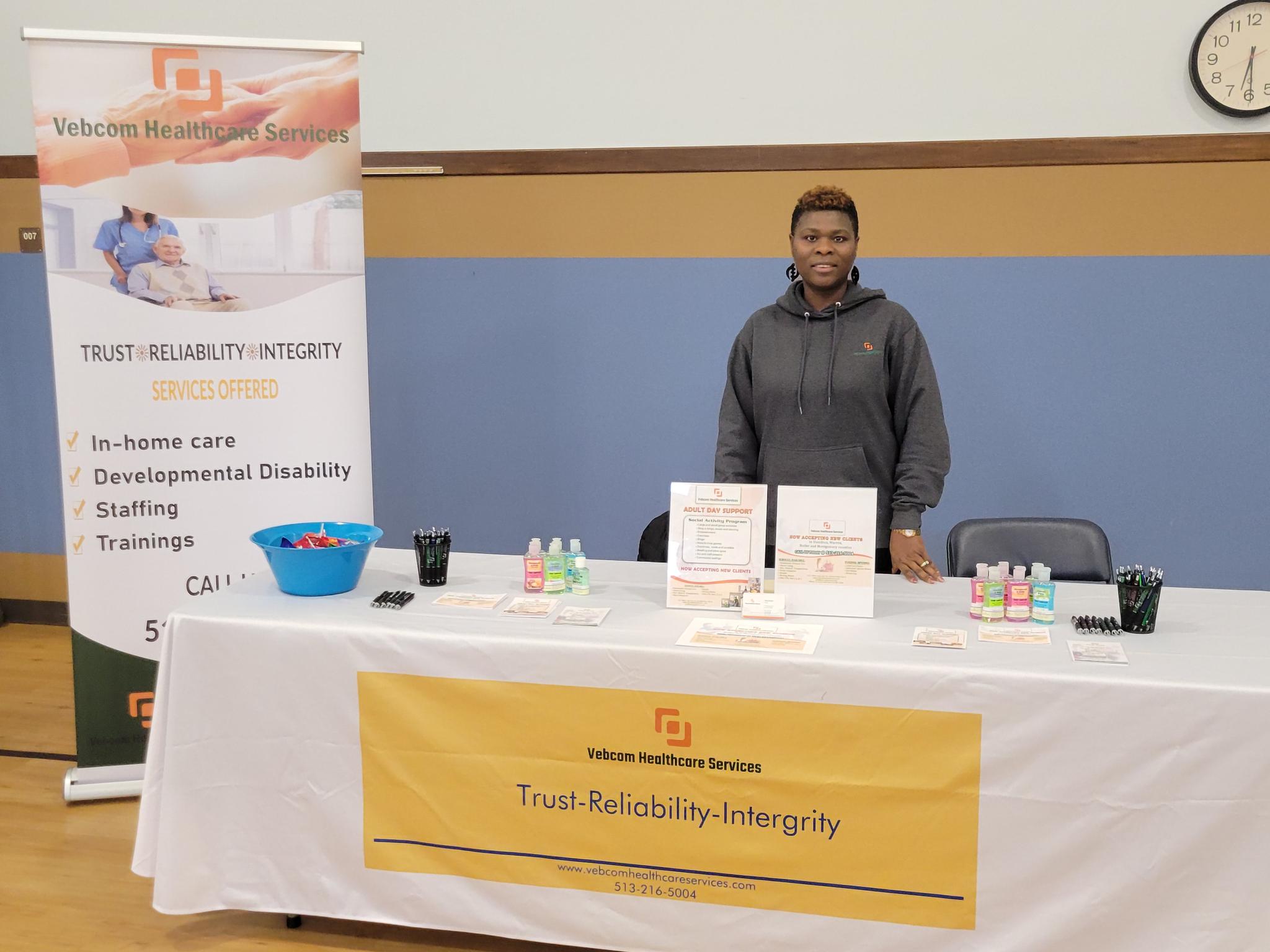 Vida Boafo standing next to a Vebcom Healthcare Services banner at the adult day center 