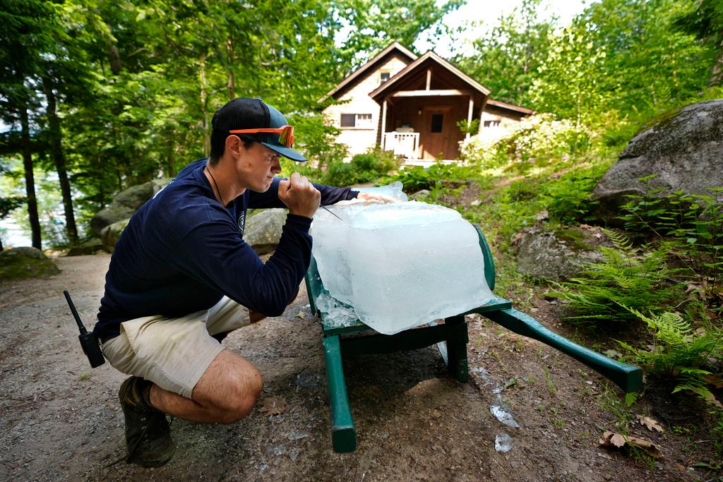 On the hottest day of the young summer season, Nate Lord uses an ice pick to break a block of ice before delivering it to a guest cabin at Rockywold Deephaven Camps, in Holderness, N.H.