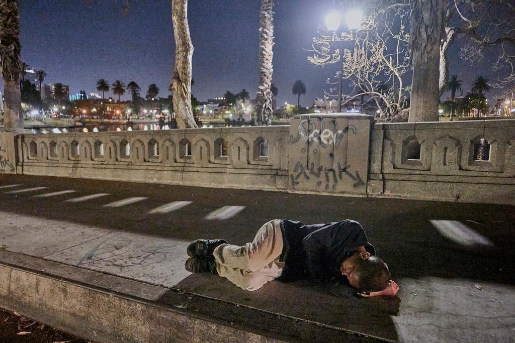A man who is homelessness sleeps on the bare sidewalk early morning at Macarthur Park in Los Angeles