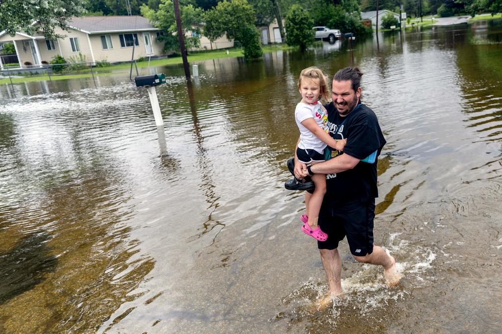 Ryan Tolbert, of Davison, carries his daughter Fiona, 4, through flood waters while walking back to their car after picking her up from his sister's house following rains from the remnants of Hurricane Beryl, Wednesday, July 10, 2024, in Genesee Township, Mich.