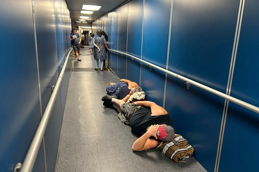 Travelers at Los Angeles International Airport sleep in a jetway for a delayed United Airlines flight to Dulles International Airport due to a widespread global outage 