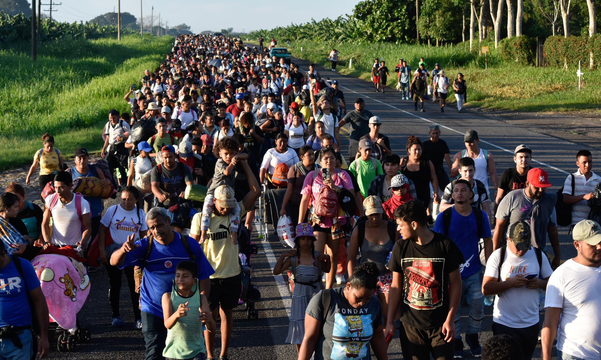 Hundreds of people walking along a grassy area on a road