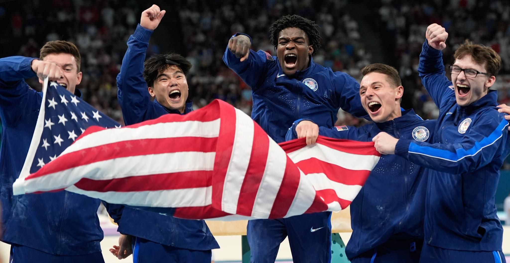 Five young men celebrating while holding the American flag and wearing blue track suits