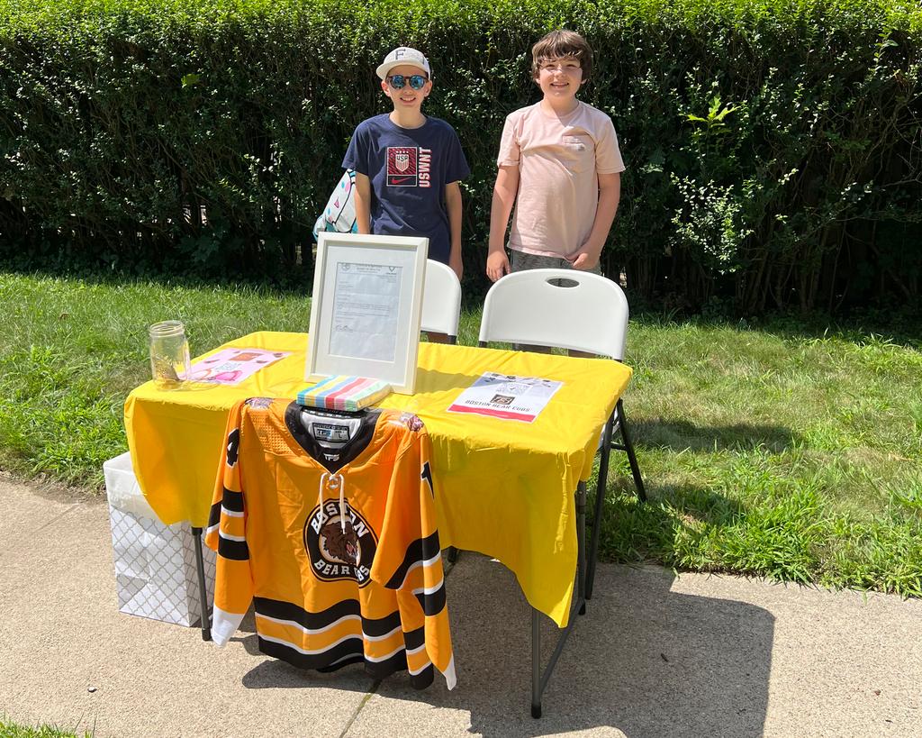 In this Saturday, Aug. 10, 2024 photo provided by Meghan Doherty, Ben Doherty, 12, of Braintree, Mass., left, stands with his cousin Danny Doherty, 12, of Norwood, Mass., right, near a table for donations to the Boston Bear Cubs hockey team, in Norwood.