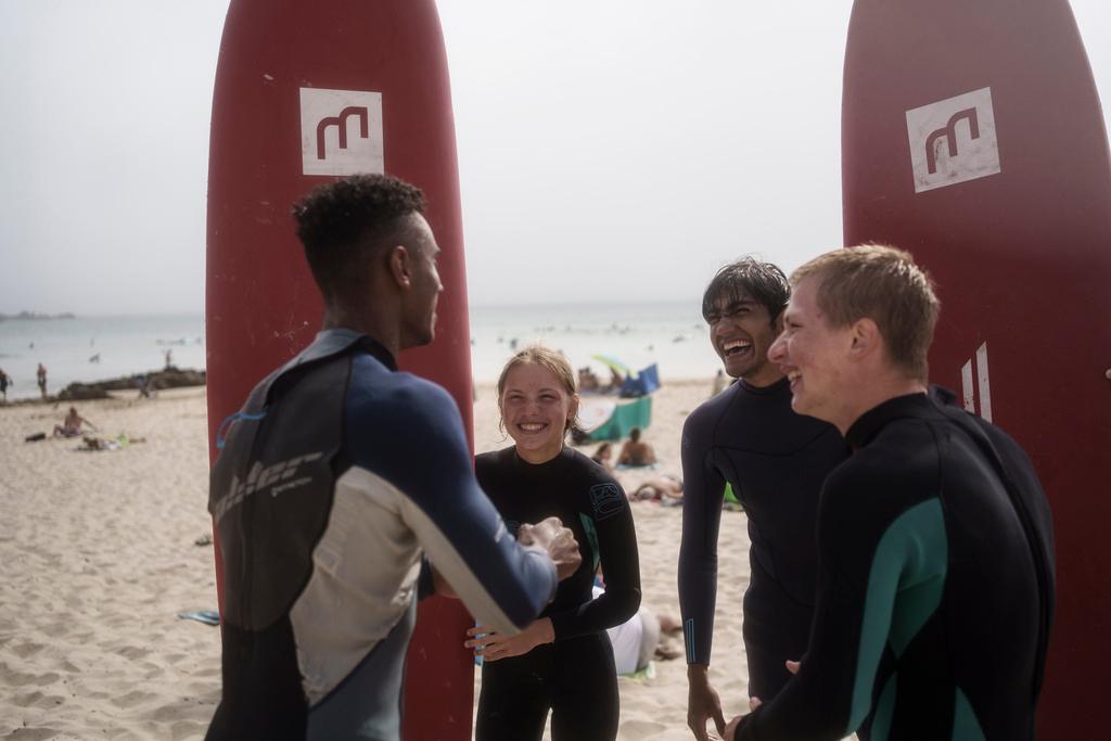 Uliana Yarova, center, laughs while on a break from surfing with other members of Surf Church Church in Matosinhos beach in the suburbs of Porto, Portugal on Sunday, Aug. 18, 2024. The Ukrainian teenager fled her war-torn country with her family after Russia's invasion and found refuge in Porto and Surf Church..
