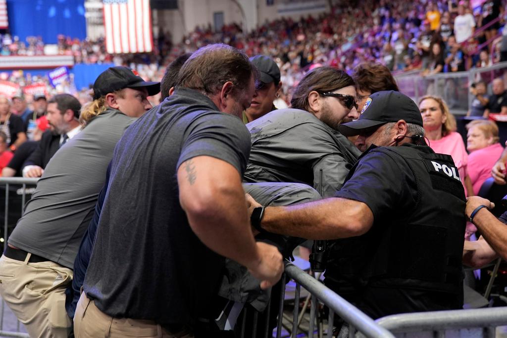 Police remove a man, center with sunglasses, who had climbed onto the media riser, as Republican presidential nominee former President Donald Trump speaks 