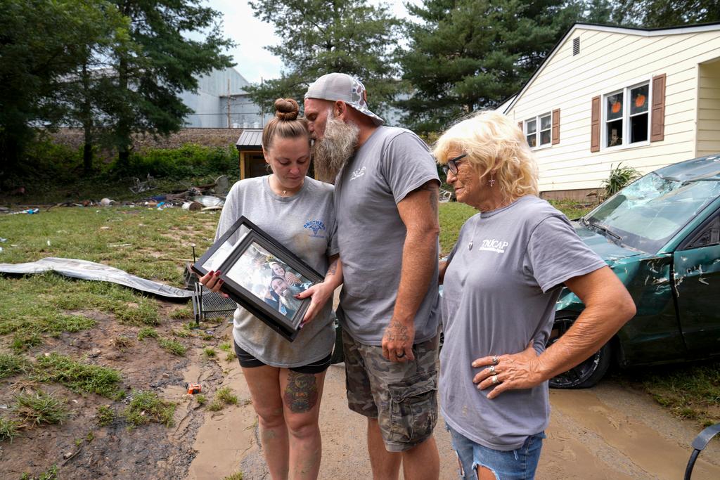 Dustin Bentley, center, kisses his wife Jennifer Bentley, left, after retrieving family photos from their flood-damaged home in the aftermatch of Hurricane Helene as his mother Janet Sams looks on in Newport, Tenn. 