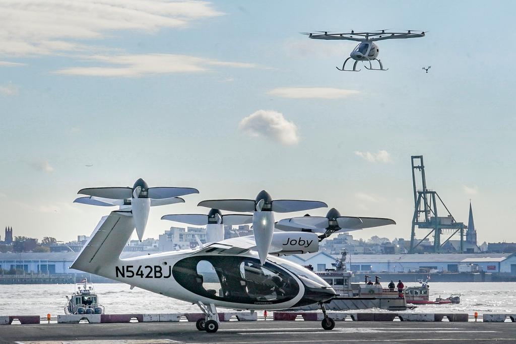 An electric vertical takeoff and landing (eVTOL) aircraft, flies above the Joby eVTOL aircraft, during a demonstration of eVTOLs 