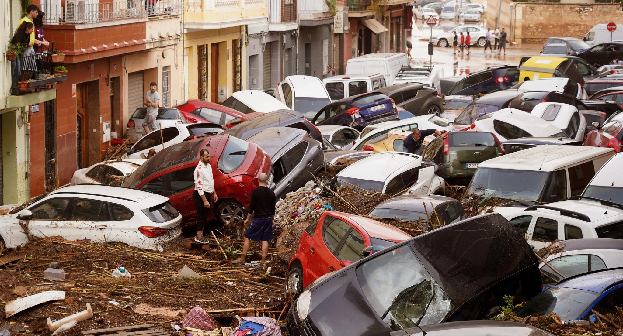 Cars piled on top of each other and wooded debris in front of apartments