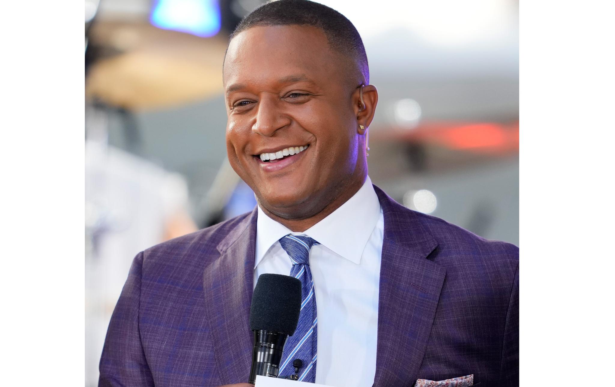 Smiling TV anchor holding a microphone, wearing suit and tie