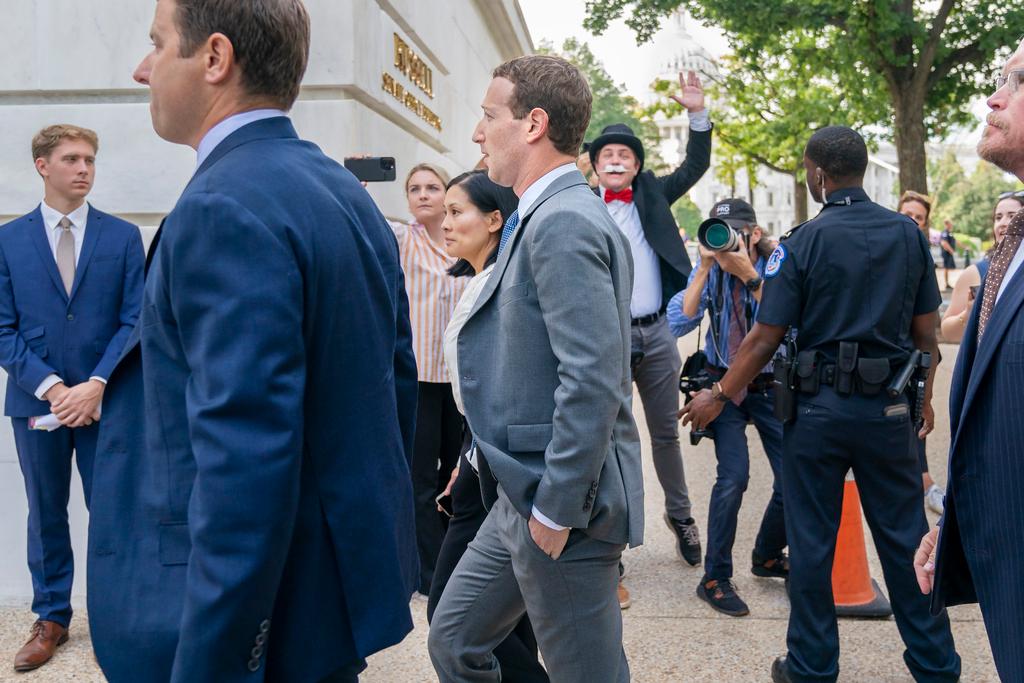 Meta CEO Mark Zuckerberg passes media and a protester as he arrives for a closed-door gathering of leading tech CEOs