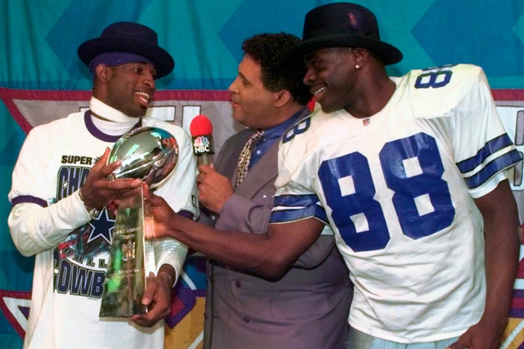 Dallas Cowboys cornerback Deion Sanders, left, and running back Michael Irvin (88) share the Vince Lombardi trophy as NBC commentator Greg Gumbel interviews the two after Super Bowl XXX