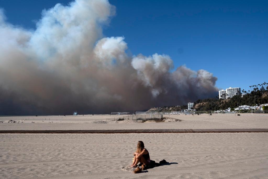 Lone sunbather sits and watches a large plume of smoke from a wildfire rise over the Pacific Palisades, in Santa Monica, Calif.
