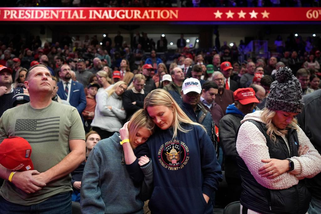 Supporters of President Donald Trump bow their heads during the invocation while watching inauguration ceremonies taking place at the U.S. Capitol on screens