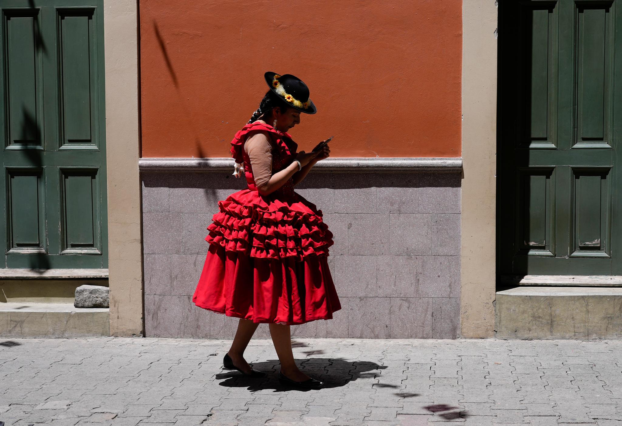 Woman in a beautiful, bright red dress and a black flat-brimmed hat, looking down at her cell phoe.