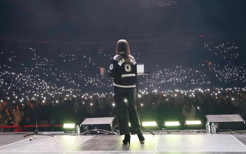 The back of a woman in front of a huge crowd with their lights brightly shining from their cell phones