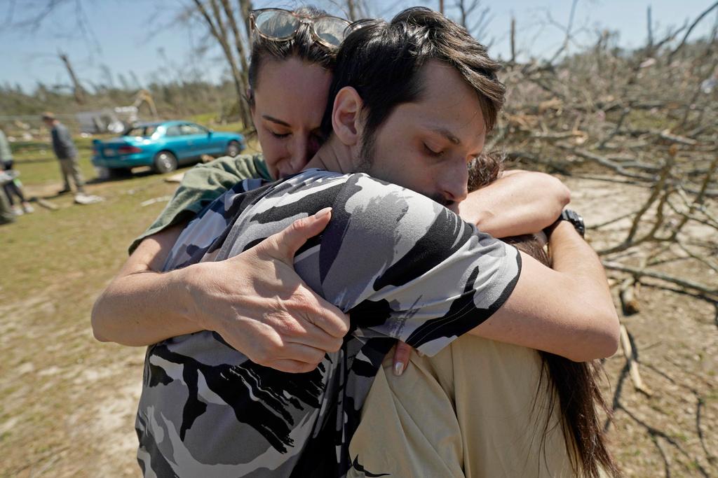 Steve Romero, 23, center, hugs his wife, Hailey Hart, right, and their friend Jessica Soileau, left, after recalling how he, his wife and their three dogs rode out Saturday's tornado in their small 1994 Toyota in Tylertown, Miss.