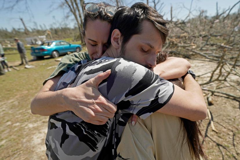 Steve Romero, 23, center, hugs his wife, Hailey Hart, right, and their friend Jessica Soileau, left, after recalling how he, his wife and their three dogs rode out Saturday's tornado in their small 1994 Toyota in Tylertown, Miss.