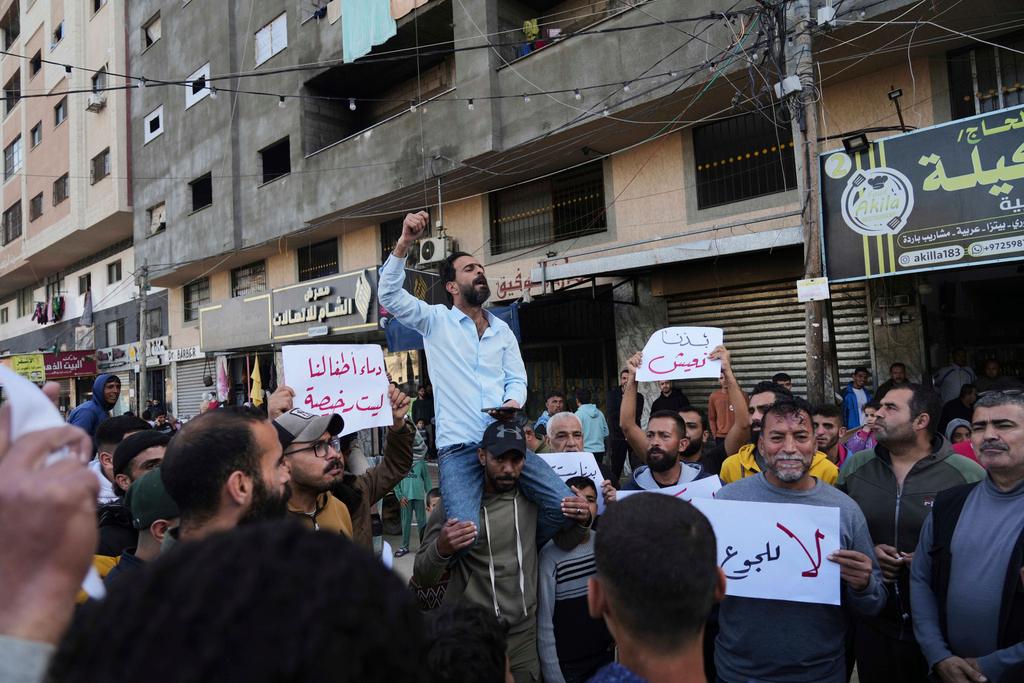 Palestinians hold signs against the war as a man chants slogans in support of the people in Bait Lahiya who came out against Hamas in a rare show of public anger against the militant group that rules the territory