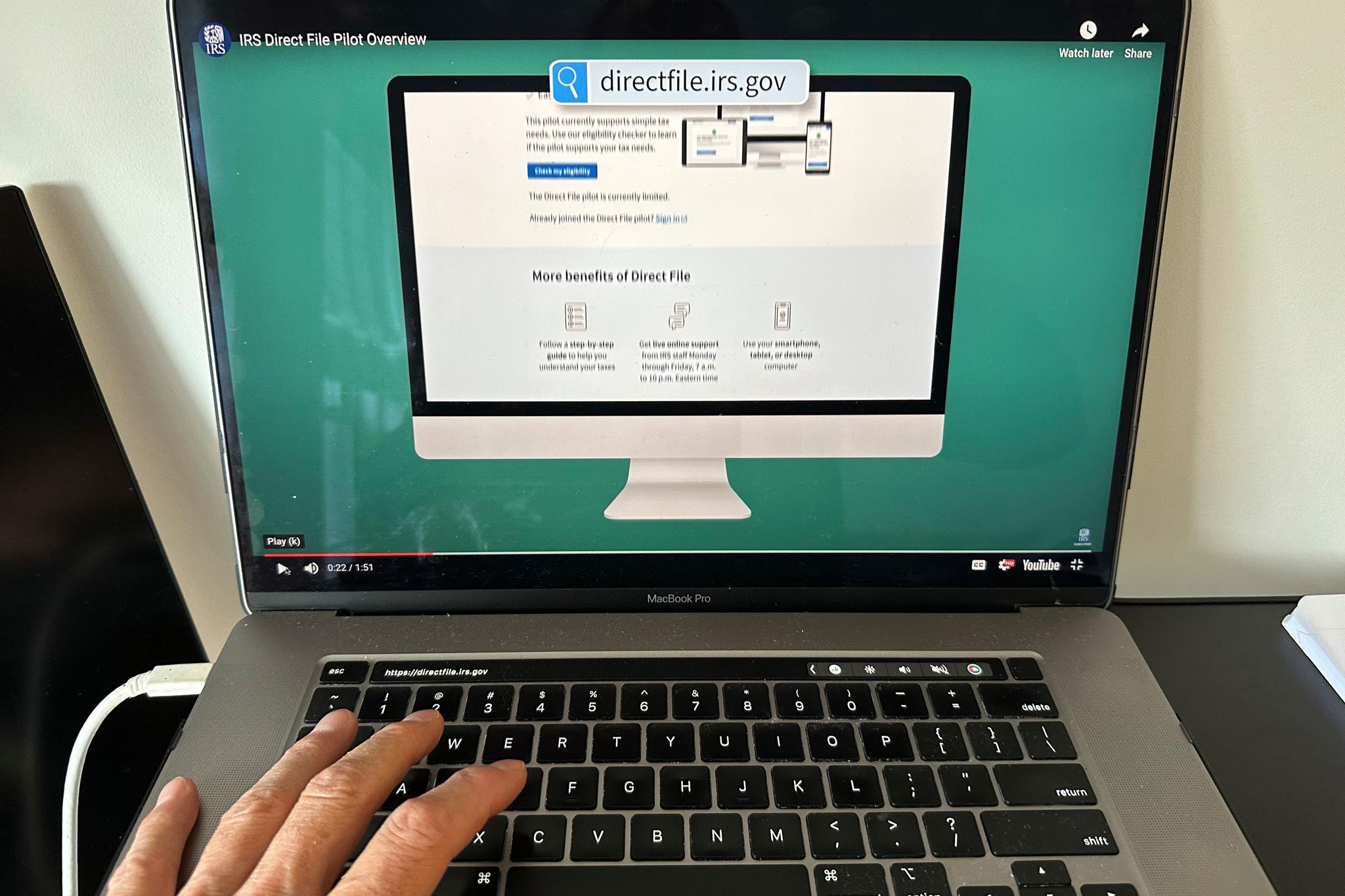A hand near a laptop with a website on the screen.