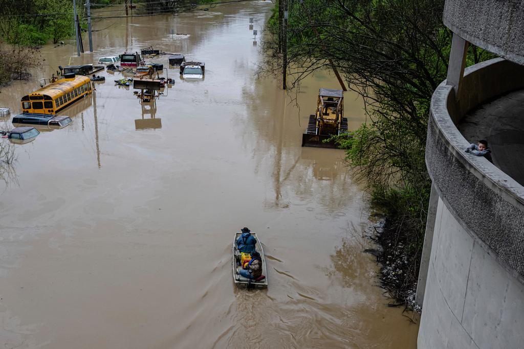 A boy looks on as people ride a boat down a flooded road in Frankfort, Ky.
